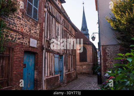 Enge Kopfsteinpflasterstraße mit Fachwerkhäusern und Kirchturm im historischen Viertel Honfleur tagsüber Stockfoto