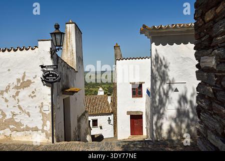Besucher spazieren durch enge Gassen in Monsaraz und erkunden traditionelle Häuser in der Region Alentejo in Portugal bei sonnigem Wetter Stockfoto