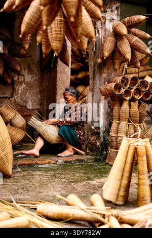 Eine ältere Frau webt Bambusfischfallen in Hanoi und zeigt in Vietnam traditionelles Handwerk und Können unter Verwendung lokaler Materialien und Techniken Stockfoto