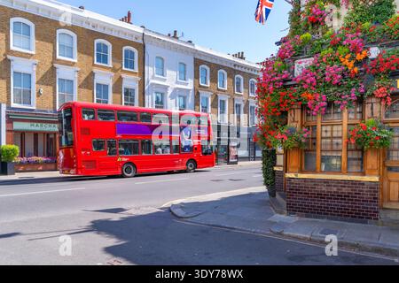 Blick auf die Churchill Arms mit hellen Blumen und einem roten Bus in Kensington an einem sonnigen Sommertag in London Stockfoto