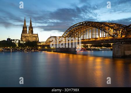 Die Hohenzollernbrücke überspannt den Rhein mit dem bei Nacht beleuchteten Kölner Dom in Nordrhein-Westfalen Stockfoto