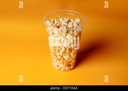 Eine volle Tasse köstliches Karamell-Popcorn wird vor einem leuchtend orangen Hintergrund präsentiert, perfekt für Snacks-Themen Stockfoto