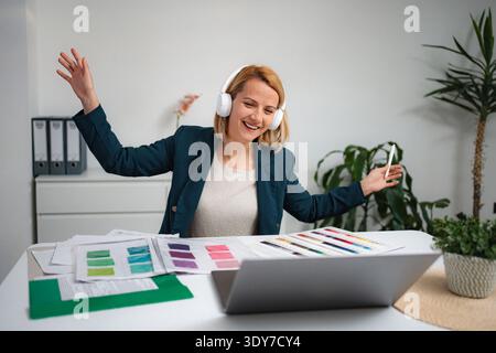 Glückliche Frau, die Musik genießt und Kopfhörer am Schreibtisch hört Stockfoto