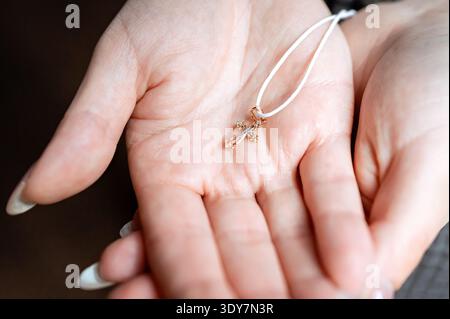 Eine Nahaufnahme von weiblichen Händen, die einen kleinen goldenen Kruzifix-Schmuck mit kleinen Diamanten oder Kristallen schröpfen. christentum, glaube, Taufzeremonie Stockfoto