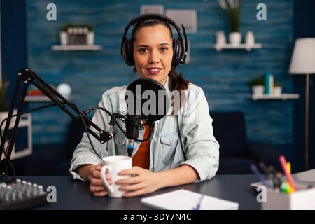 Vlogger sendet ihr Publikum, während sie im Heimstudio Podcasts für soziale Medien macht. Blogger, die Online-Talkshow mit Kopfhörern aufnehmen, professionelles Mikrofon, das während der Übertragung auf die Kamera blickt. Stockfoto