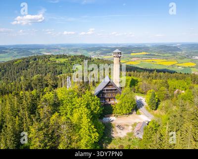 Erkunden Sie den atemberaubenden Blick aus der Luft auf den Svatobor Aussichtsturm in Tschechien, umgeben von üppigen Wäldern und sanften Hügeln unter einem klaren blauen Himmel, der natürliche Schönheit und architektonischen Charme bietet. Stockfoto