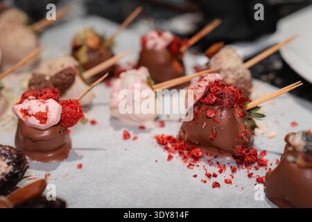 Nahaufnahme von handgefertigten Erdbeeren mit Schokoladenüberzug, verziert mit verschiedenen Belägen und Streuseln auf Backpapier. Gourmet-Dessert-Konzept, Konfekt Stockfoto