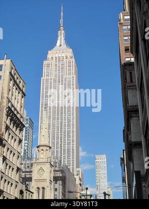 Ein Blick auf die Straße in Midtown Manhattan, New York City, zeigt das Empire State Building, das sich vor klarem Himmel erhebt. Stockfoto