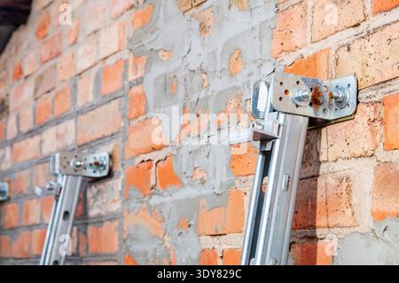 Nahaufnahme der Metallbefestigungen, die an einer rauen Ziegelwand befestigt sind, zeigt laufende Bau- oder Reparaturarbeiten an Stockfoto