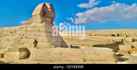 Große Sphinx-Statue in der Nekropolis von Gizeh unter blauem Himmel mit alter Pyramide, berühmtes ägyptisches Wahrzeichen. Stockfoto