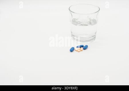 Glas Wasser mit mehreren Pillen auf einer weißen Oberfläche, minimales sauberes Stillleben. Stockfoto
