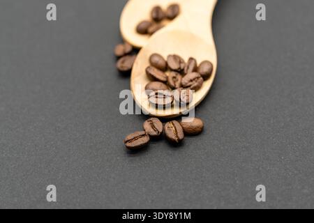 Nahaufnahme gerösteter Kaffeebohnen in Holzlöffeln auf dunklem, strukturiertem Hintergrund Stockfoto