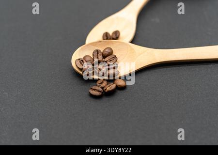 Kaffeebohnen in Holzlöffeln auf dunklem Hintergrund, Nahaufnahme, rustikale Minimalkomposition Stockfoto
