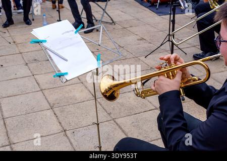 Detail eines sitzenden Mannes, der in Schwarz gekleidet ist und Trompete mit Noten vor sich spielt. Stockfoto