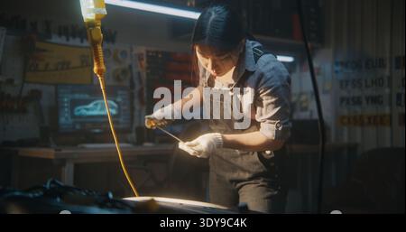 Automatische Mechanikerin, Buchse, die den Ölstand mit dem Messstab in der Werkstatt prüft. Woman Focus zieht den Ölmessstab heraus und wischt ihn vorsichtig mit einem Tuch ab, um eine genaue Ablesung zu gewährleisten. Überwachung und präventive Car Care. Stockfoto