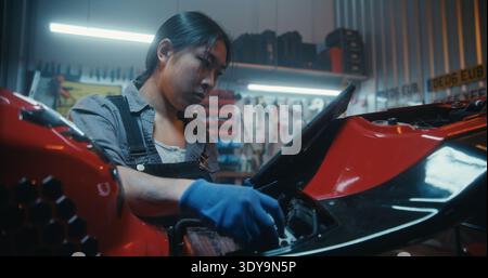 Tablet Für Junge Frauen Mit Digitalem Schaltplan. Frau Vergleicht Das Schema Beim Anschließen Der Motorradbatterie An Das Steuergerät Sorgfältig. Moderner Ansatz Motorradreparatur Mit Digitalen Werkzeugen. Stockfoto