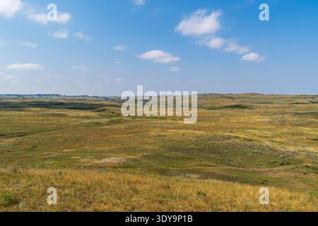 Die weitläufige Prärie öffnet sich in die zerklüfteten Badlands des Grasslands National Park unter hellem, sonnigem Himmel. Stockfoto