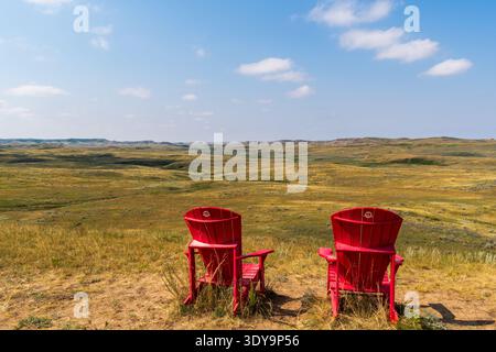 Fire Mountain, SK CANADA - 6. August 2024: Rote Stühle von Park's Canada mit Blick auf die Landschaft der Prärie-Badlands. Stockfoto