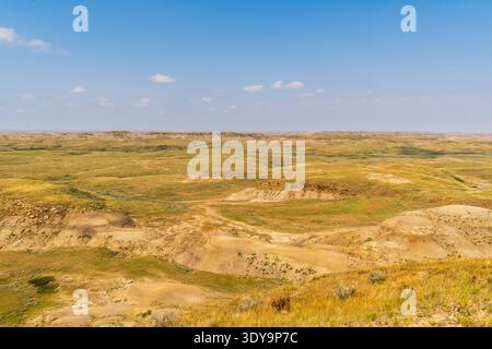 Buttes und freiliegende Erdschichten schaffen eine dramatische Landschaft, geätzt von Erosion und eingerahmt von hellblauem Himmel. Stockfoto