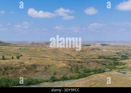 Die erodierten Grasslands und farbenfrohen Schichten des East Block Badlands erheben sich unter einem klaren blauen Himmel aus der Prärie. Stockfoto