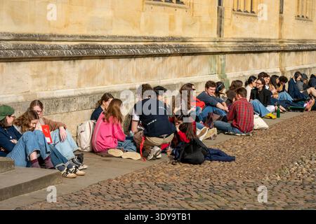 Gruppe junger Studenten, die an einer Mauer im historischen Stadtzentrum von Oxford sitzen, während sie einen Tagesausflug in die Universitätsstadt Unternehmen. Stockfoto