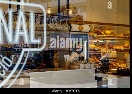 Barcelona - Spanien - 11. April 2022. Blick von außen auf das Innere eines Cafés und einer Bäckerei mit einer Frau, die hinter der Theke serviert. Stockfoto