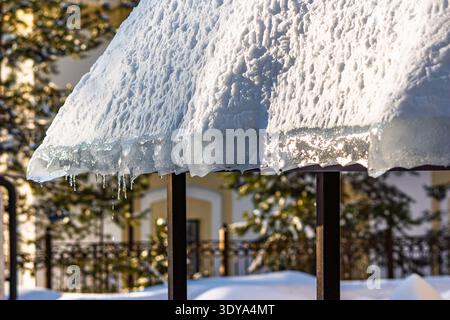 Schmelzender Schnee und Eis überhängen an einer Dachkante mit sonnendurchfluteten Eiszapfen, die im Spätwinter oder Frühjahrs-Tauen tropfen Stockfoto