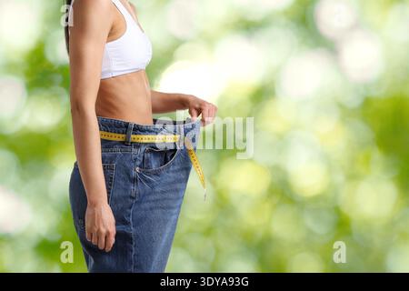 Frau in ihrer alten Jeans vor verschwommenem grünem Hintergrund, Nahaufnahme. Gewichtsverlust Stockfoto