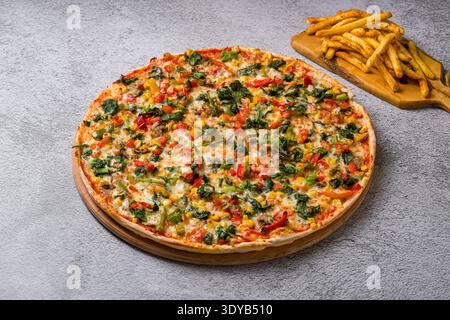 Spinatpizza mit farbenfrohem Gemüse und knusprigen Pommes frites auf dem Tisch Stockfoto