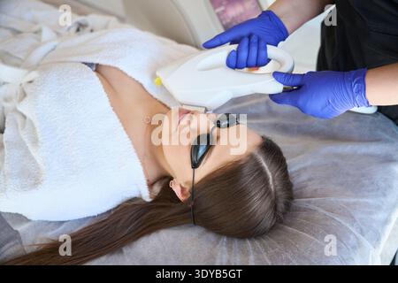 Frau in Bademantel und Schutzbrille, die während des Schönheitsverfahrens auf der Couch liegt Stockfoto
