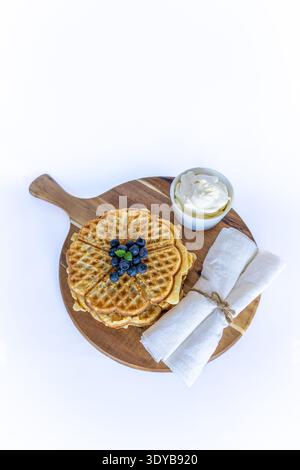 Schwedische Waffeln in Herzform mit frischen Blaubeeren und Schlagsahne auf einem Holzbrett Stockfoto