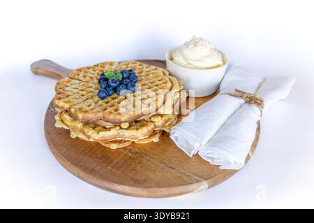 Schwedische Waffeln in Herzform mit frischen Blaubeeren und Schlagsahne auf einem Holzbrett Stockfoto