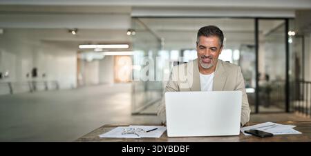 Glücklicher Geschäftsmann mittleren Alters, der am Schreibtisch am Computer arbeitet. Stockfoto