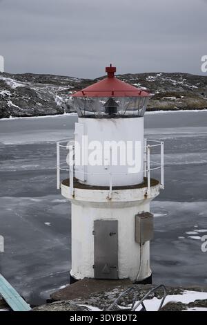 Kleiner weißer Leuchtturm mit rotem Dach an der gefrorenen Küste von Mollsund, Schweden. Nordisches Schifffahrtszeichen in einer Winterlandschaft mit Eis und Schnee Stockfoto