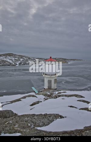 Kleiner weißer Leuchtturm mit rotem Dach an der gefrorenen Küste von Mollsund, Schweden. Nordisches Schifffahrtszeichen in einer Winterlandschaft mit Eis und Schnee Stockfoto