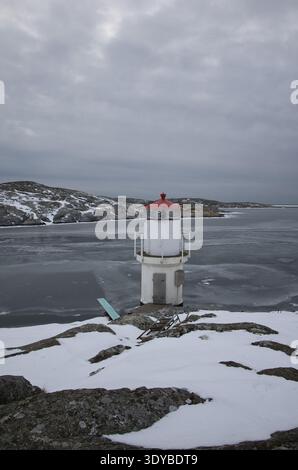 Kleiner weißer Leuchtturm mit rotem Dach an der gefrorenen Küste von Mollsund, Schweden. Nordisches Schifffahrtszeichen in einer Winterlandschaft mit Eis und Schnee Stockfoto