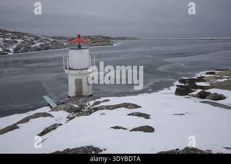 Kleiner weißer Leuchtturm mit rotem Dach an der gefrorenen Küste von Mollsund, Schweden. Nordisches Schifffahrtszeichen in einer Winterlandschaft mit Eis und Schnee Stockfoto