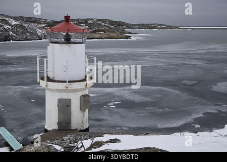 Kleiner weißer Leuchtturm mit rotem Dach an der gefrorenen Küste von Mollsund, Schweden. Nordisches Schifffahrtszeichen in einer Winterlandschaft mit Eis und Schnee Stockfoto