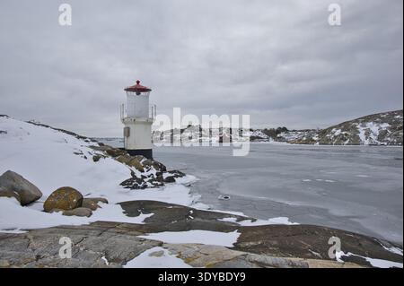 Kleiner weißer Leuchtturm mit rotem Dach an der gefrorenen Küste von Mollsund, Schweden. Nordisches Schifffahrtszeichen in einer Winterlandschaft mit Eis und Schnee Stockfoto