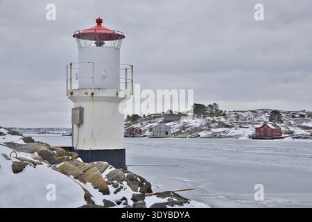Kleiner weißer Leuchtturm mit rotem Dach an der gefrorenen Küste von Mollsund, Schweden. Nordisches Schifffahrtszeichen in einer Winterlandschaft mit Eis und Schnee Stockfoto