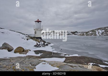 Kleiner weißer Leuchtturm mit rotem Dach an der gefrorenen Küste von Mollsund, Schweden. Nordisches Schifffahrtszeichen in einer Winterlandschaft mit Eis und Schnee Stockfoto
