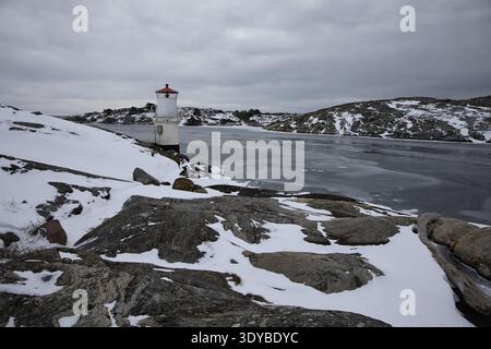 Kleiner weißer Leuchtturm mit rotem Dach an der gefrorenen Küste von Mollsund, Schweden. Nordisches Schifffahrtszeichen in einer Winterlandschaft mit Eis und Schnee Stockfoto