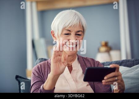 Videoanrufe, glückliche und ältere Frau auf dem Sofa für Gespräche, Gespräche und soziale Netzwerke. Ruhestand, Hallo und ältere Person auf Smartphone-Welle Stockfoto