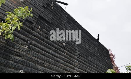 Verbrannte Baumstämme einer hölzernen Hauswand, die Brandschäden und Zerstörung zeigen Stockfoto