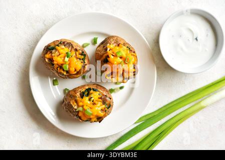 Leckere gefüllte gebackene Kartoffeln mit Pilzen, Spinat, karamelisierten Zwiebeln und Cheddar-Käse serviert mit Joghurtsauce auf hellem Steinhintergrund. Stockfoto