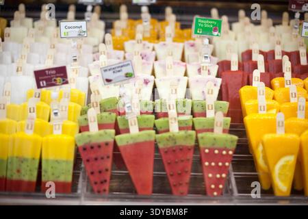 Reihen von farbenfrohen, handgefertigten Fruchteis auf Holzstäben im Glasvitrinen, mit Wassermelonen-Kiwi und Mango-Aromen für den Sommereinzelhandel. Stockfoto