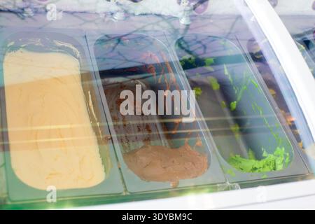 Verschiedene Eisaromen wie Vanille, Schokolade und Pistazien in Edelstahlschalen in einer gekühlten Vitrine in einem Dessertsalon. Stockfoto
