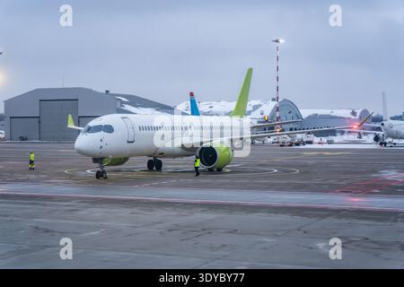 Passagierjet parkte auf dem Vorfeld des Winterflughafens mit Bodenbesatzung in gut sichtbarer Ausrüstung, Pistenmarkierungen und Terminalgebäude dahinter, Flugzeuglogik Stockfoto
