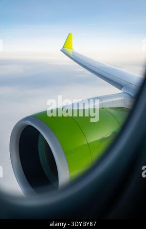 Passagierflugzeug-Triebwerk-Maschinenhaus in hellgrüner Farbe vom Fenster aus gesehen mit Flügel, der sich über Wolkendeck erstreckt, kommerzieller Flug in großer Höhe, Transportaten Stockfoto