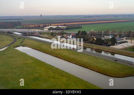 Höhenpanorama über die Niederlande mit Entwässerungskanal neben der Autobahn, grünen Ackerflächen und ländlichen Häusern, die die Infrastruktur-pla veranschaulichen Stockfoto